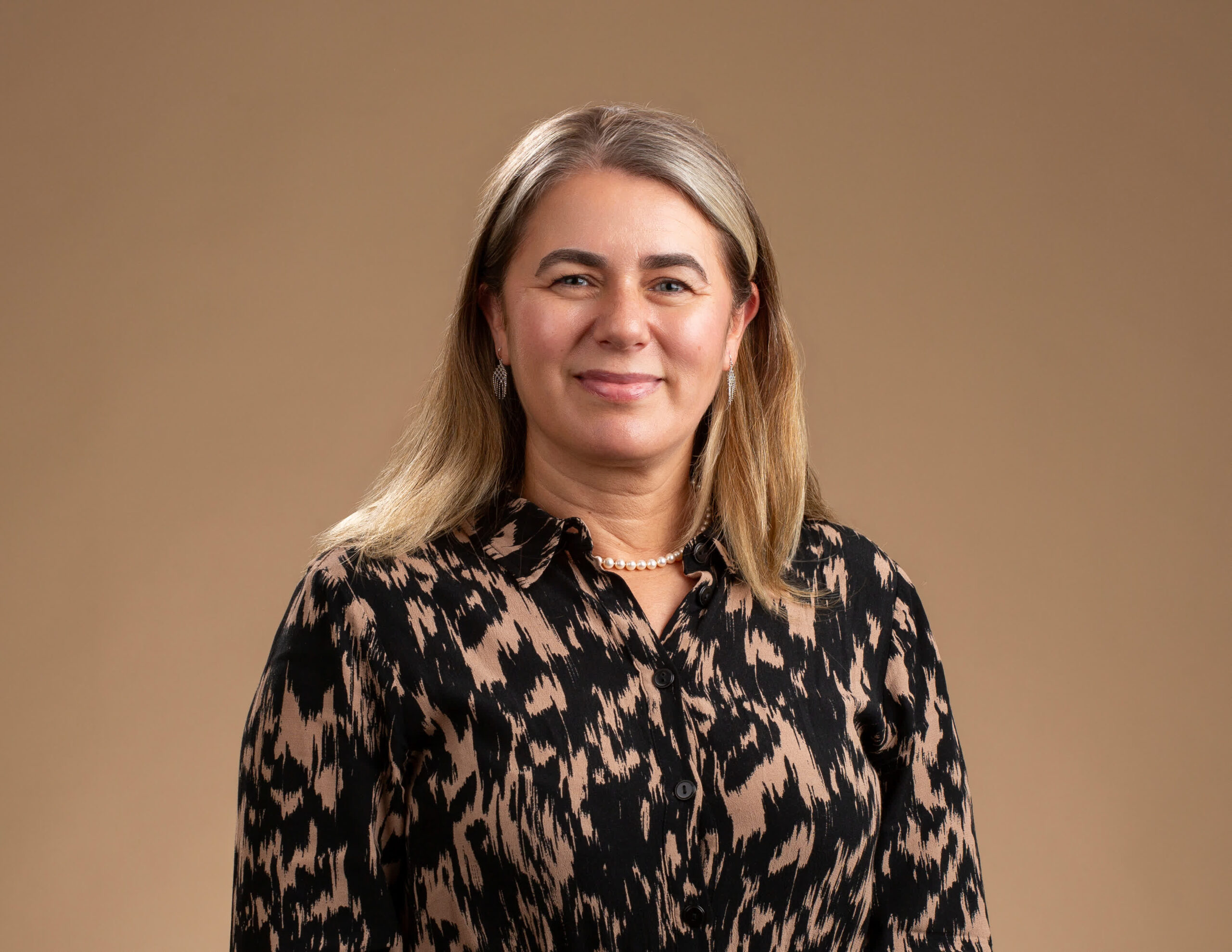 Portrait of Dr. Guelay Bilen-Rosas wearing a patterned blouse and pearl necklace against a neutral background.