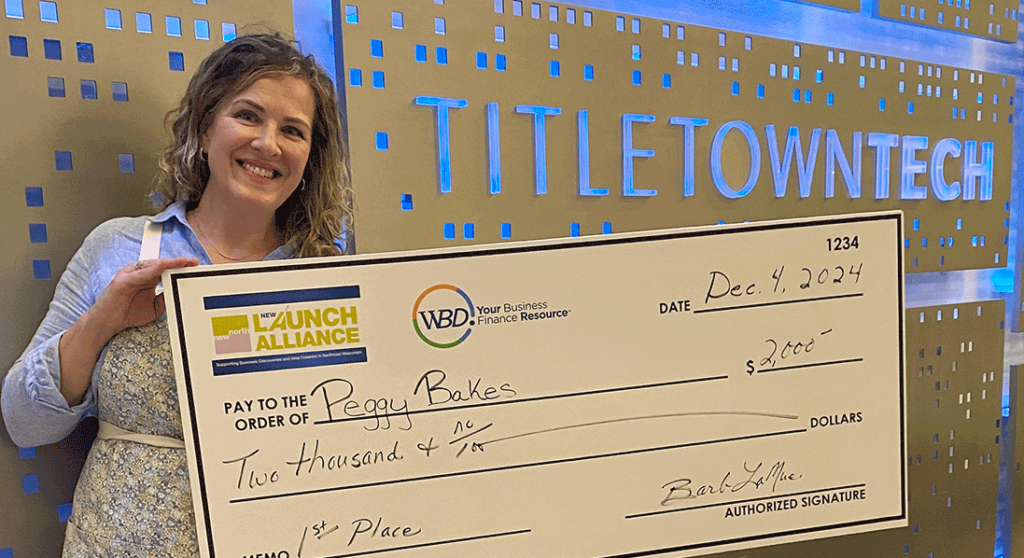 woman business owner holding large check in front of sign Titletown Tech